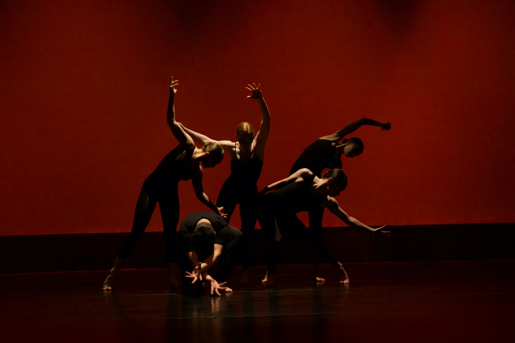 Grupo de bailarinos de preto em cena contra um fundo vermelho
