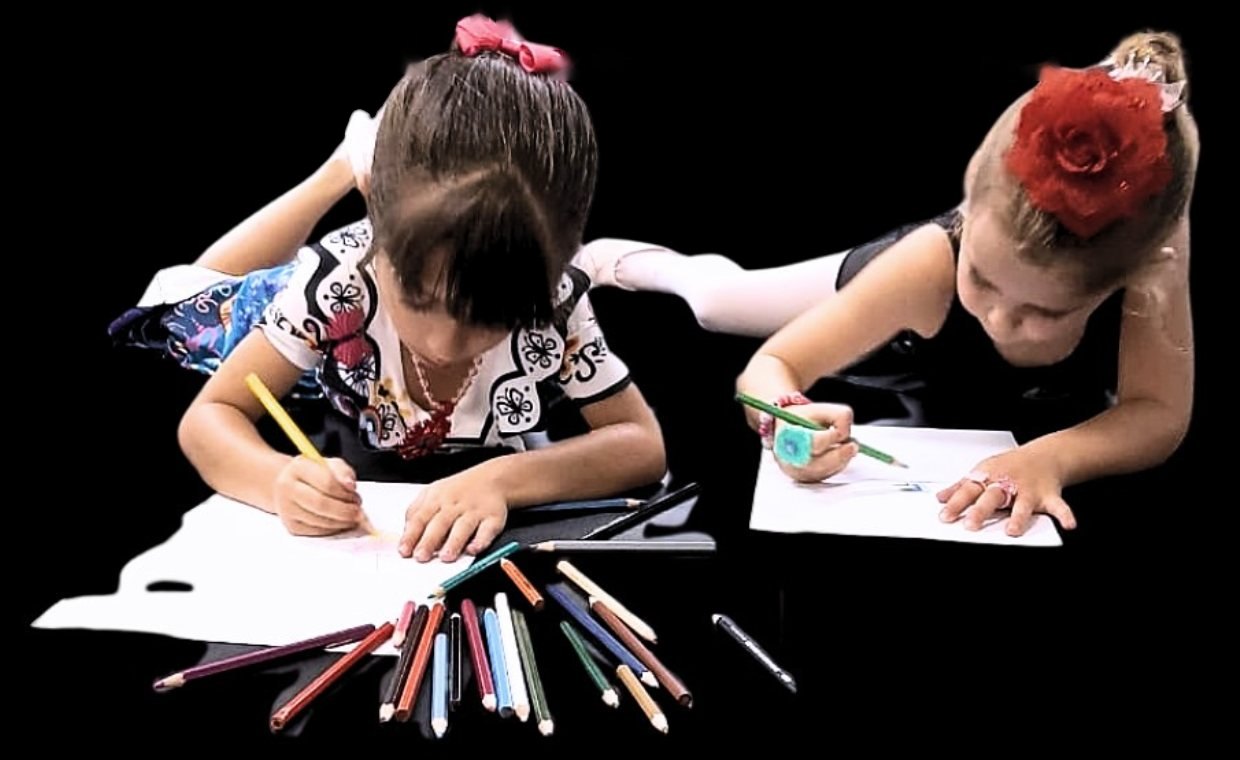 Duas alunas pequenas deitadas no chão desenhando com lápis de cor