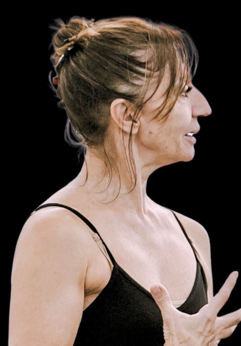 Professora de perfil, de cabelo preso, explicando um movimento