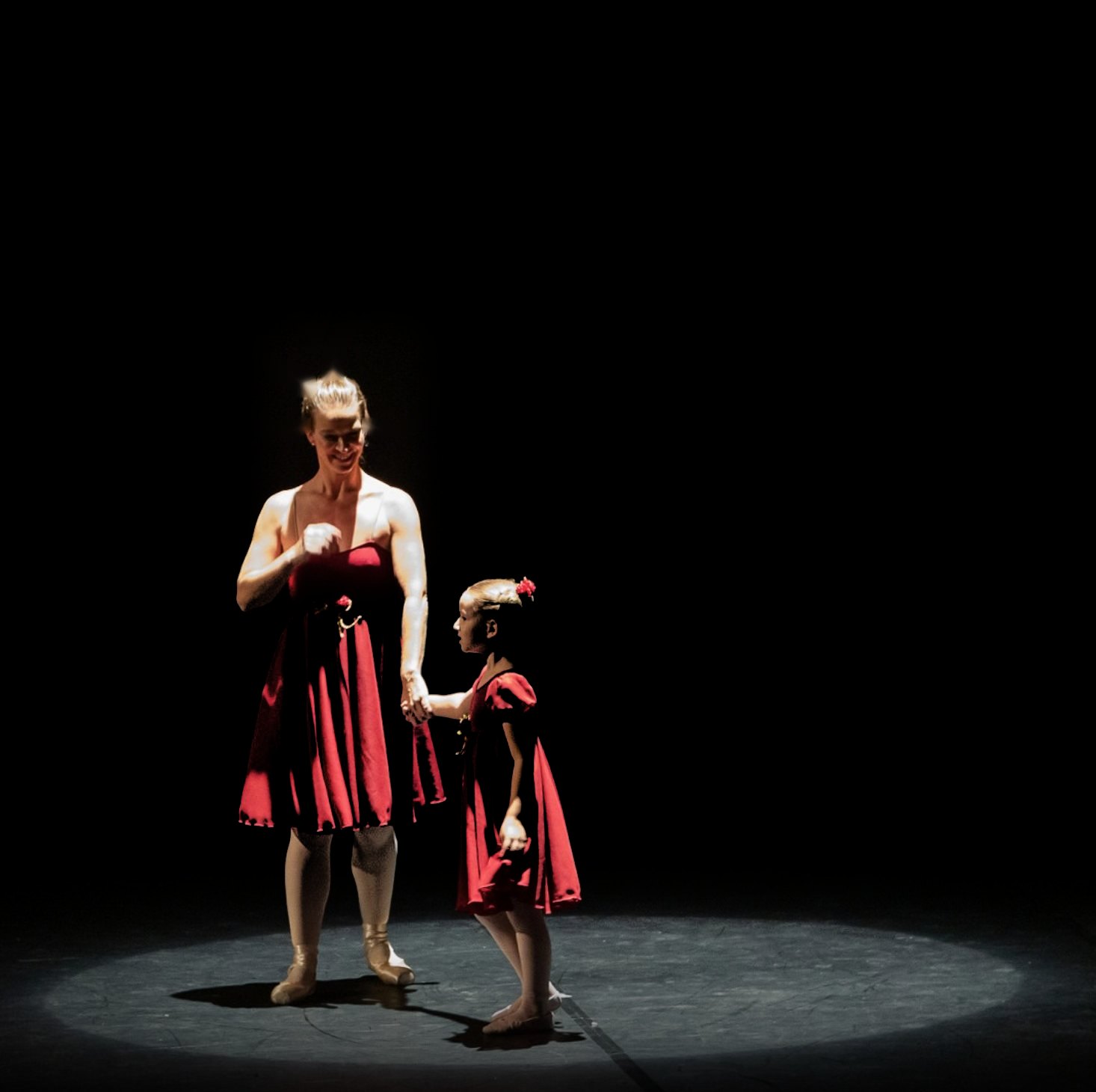 Bailarina e aluna de vestido vermelho, de mãos dadas sob o foco de luz no palco